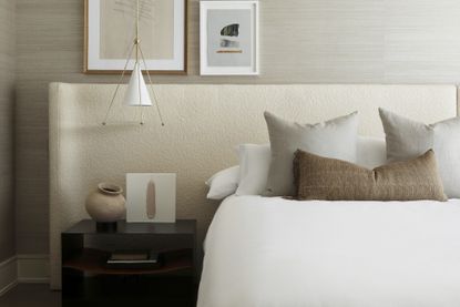 neutral bedroom ideas with boucle headboard, pendant light, artwork, black side table, vase, pillows