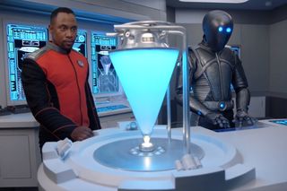 Isaac (Mark Jackson) and LaMarr (J. Lee) tinker with a time travel device that looks suspiciously like an elaborate snow-cone maker.