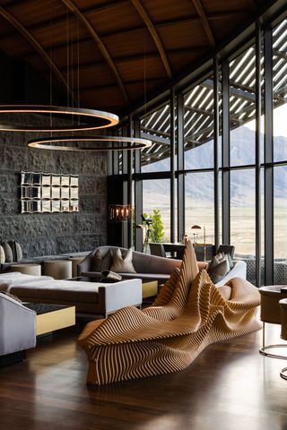 A minimalist moutain hotel features linear furniture in neutral tones juxtaposed with statement pieces such as a wavy bench in textural wood.