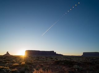 stages of the annular solar eclipse rise through the blue sky above large rock formations.