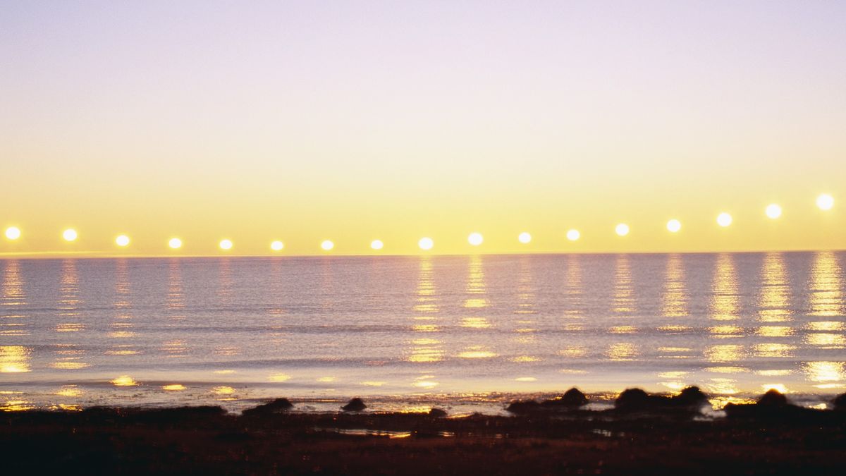 image showing multiple exposures of the sun as it dips close to the horizon and then begins to rise again, it is reflected on the water below. 