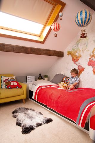 A child's bedroom with map wall mural, red and white bed covers and a yellow armchair