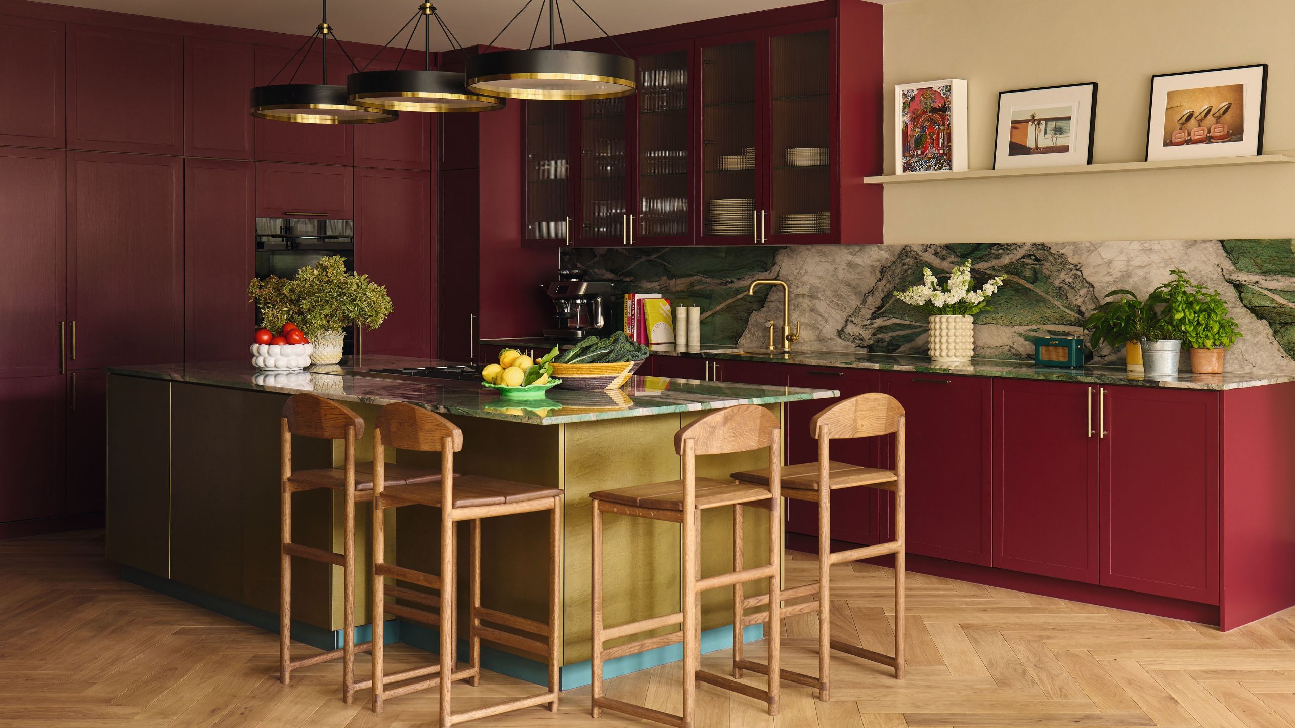 a bright red pink traditional shaker kitchen with statement green veined marble counters and backsplash, a green island with mid century wooden stools and contemporary round pendants hung above