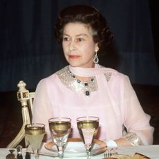 Queen Elizabeth wearing a pink dress sitting at a dining table