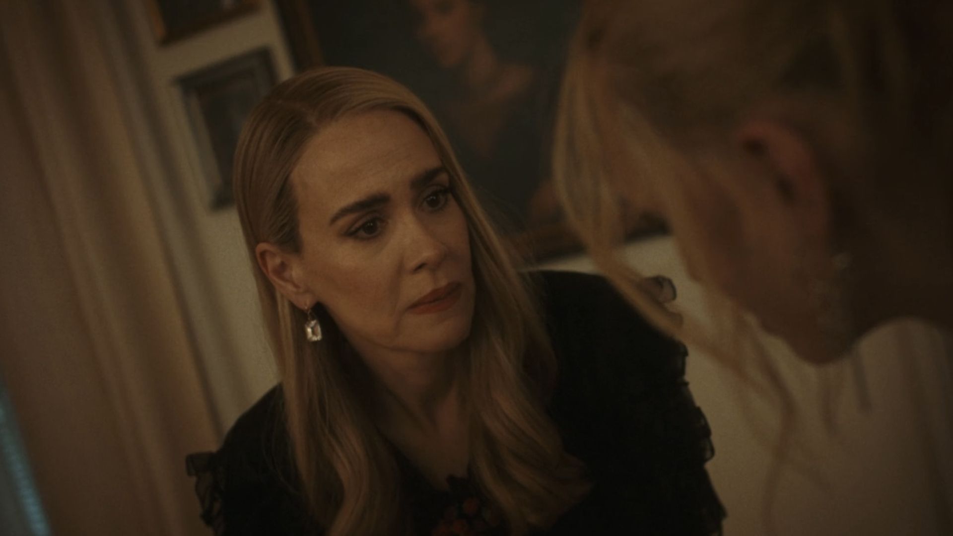 Cordelia in a black dress talking to Morwenna in the Coven house.