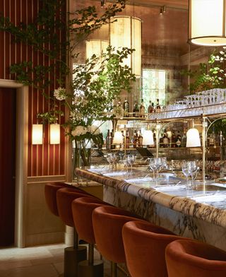 A mid-century modern decorated restaurant features glass lighting exuding warm, yellow light, brick-colored, stripy walls, marble counters, and luxurious accessories.