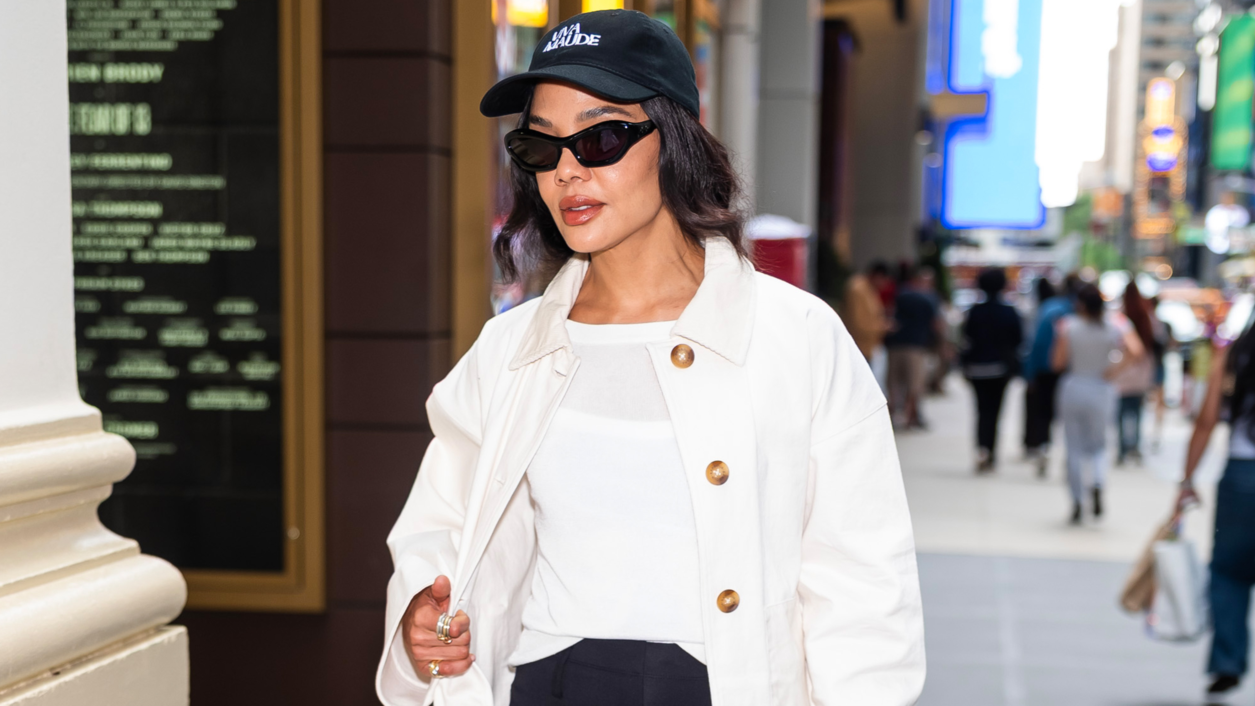 Tessa thompson wears a black baseball cap, white barn jacket, and a white tee.