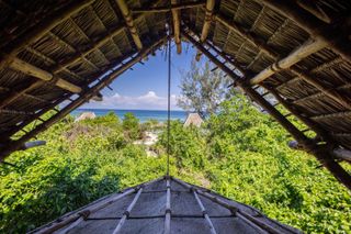 A wood and rattan bungalow oversees a lush forest leading into the blue of the sea.