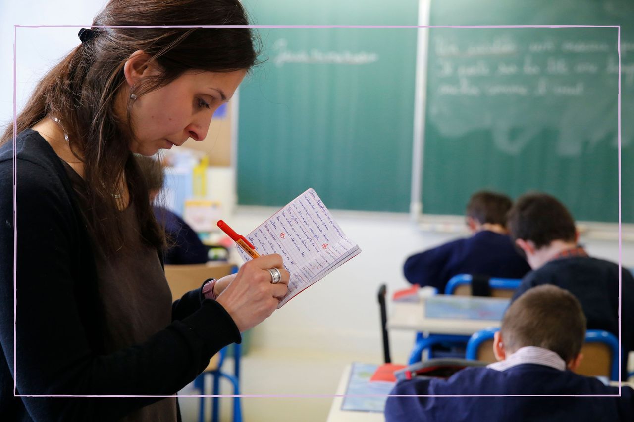 Teacher writing in a book while students in class