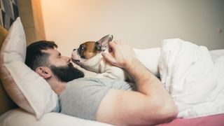 Man cuddling dog in bed in the morning