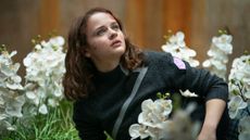 Joey King as Tally with blood on her face and lying in a bed of white orchids in Uglies.