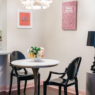 Small white-top round dining table in small apartment with black dining chairs and small bouquet plus colorful framed prints behind