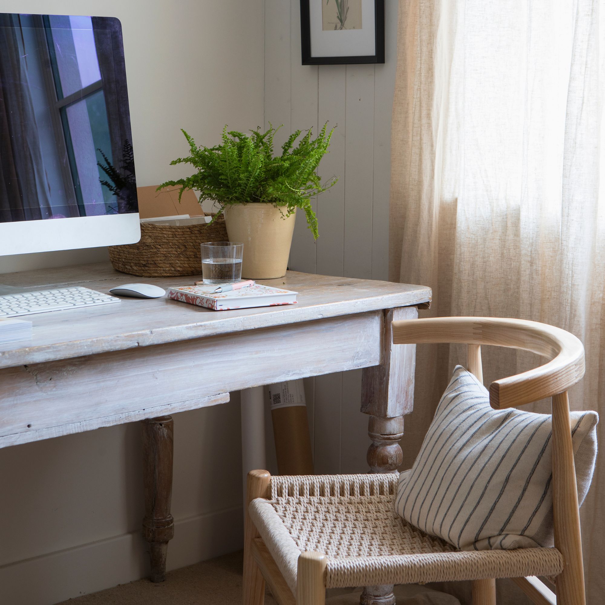 Home office with a wooden desk and wicker chair, and a computer and plant on the desk