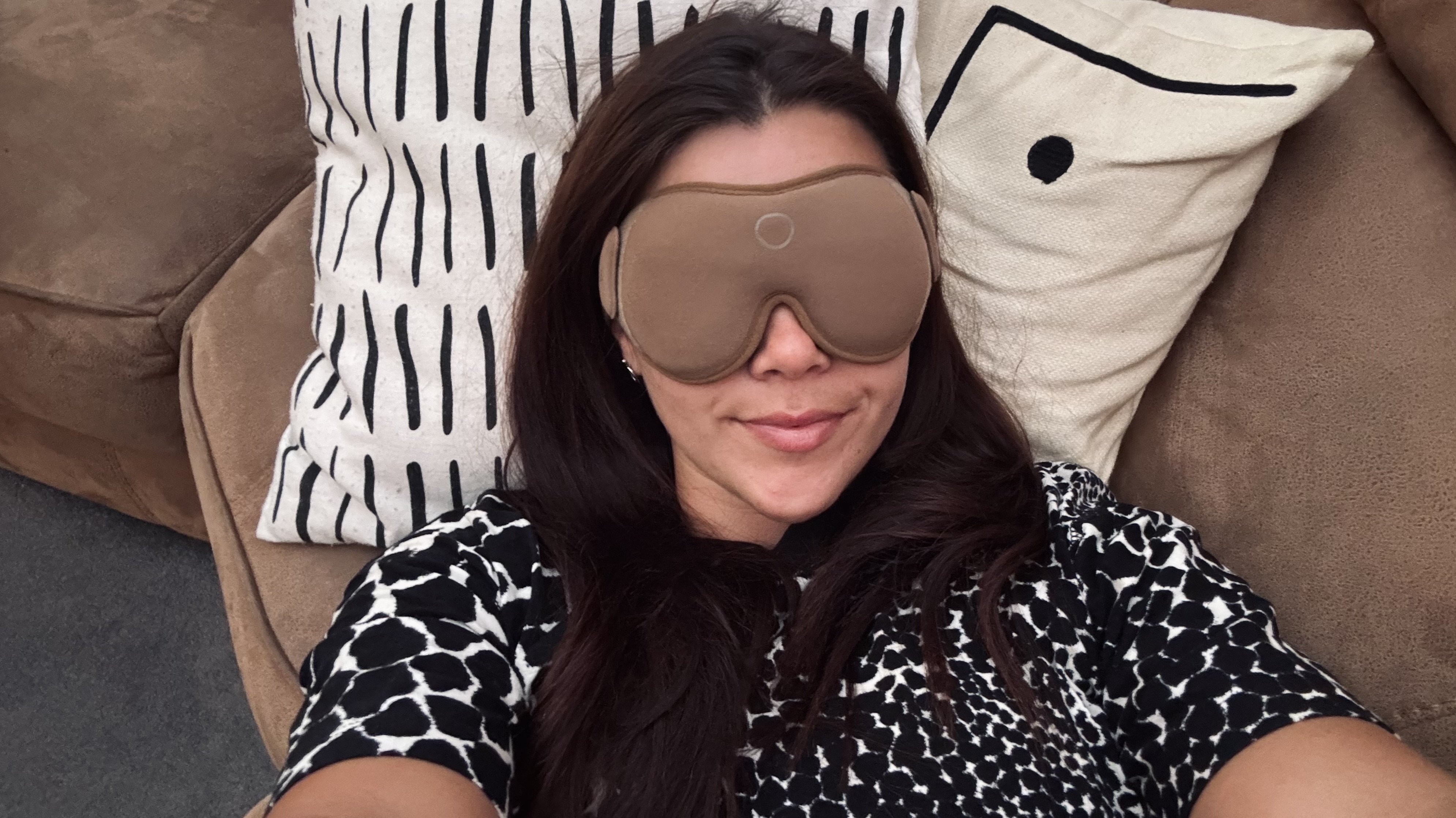 A girl wearing a black and white top wearing the beige SOMO sleep mask laying on sofa for a nappuccino