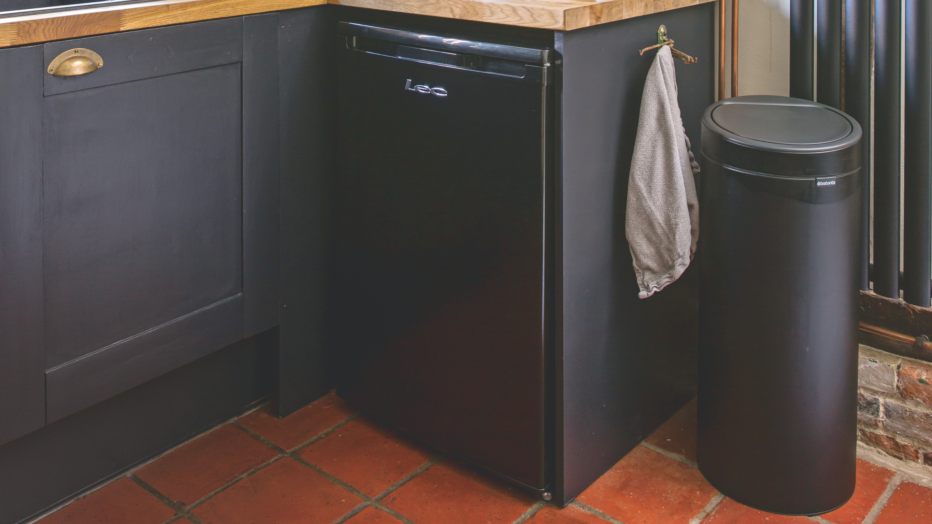 Black kitchen bin on red tiled floor, next to black kitchen cabinets.