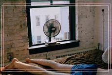 A fan on a windowsill and the back of a man's legs on a bed