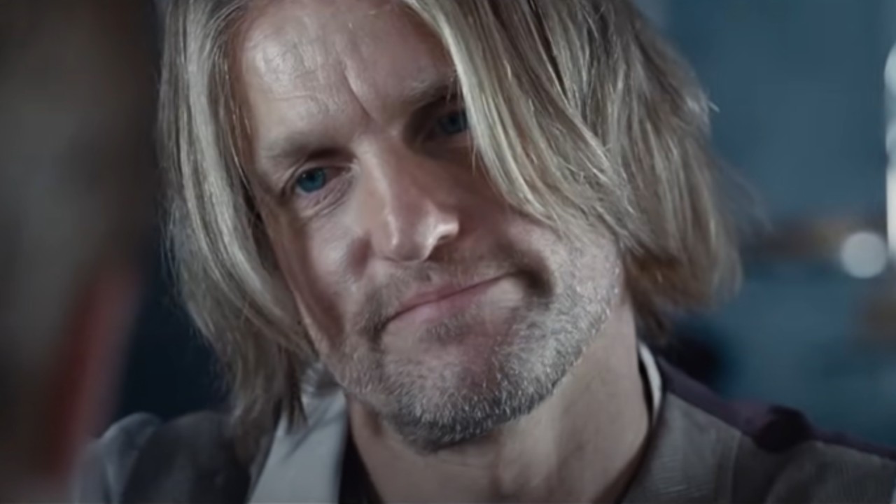 Açlık Oyunları'nda Woody Harrelson'ın Haymitch rolünde, yüzünde saç var ve sırıtıyor.