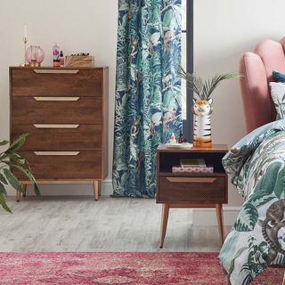 Dunelm Anya Bedside Table with a tiger vase on top of it, in a bedroom with bed and chest of drawers and tropical curtains