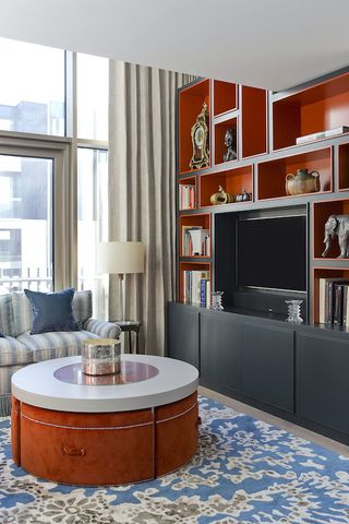 living room with orange and black bookcase with tv blue rug and orange pouffe