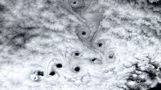A satellite photo sowing ten dark holes in the clouds swirling in the sky