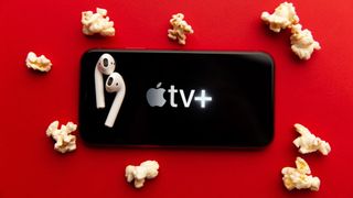 Image showing the Apple TV Plus logo on a mobile phone with a pair of AirPods surrounded by popcorn