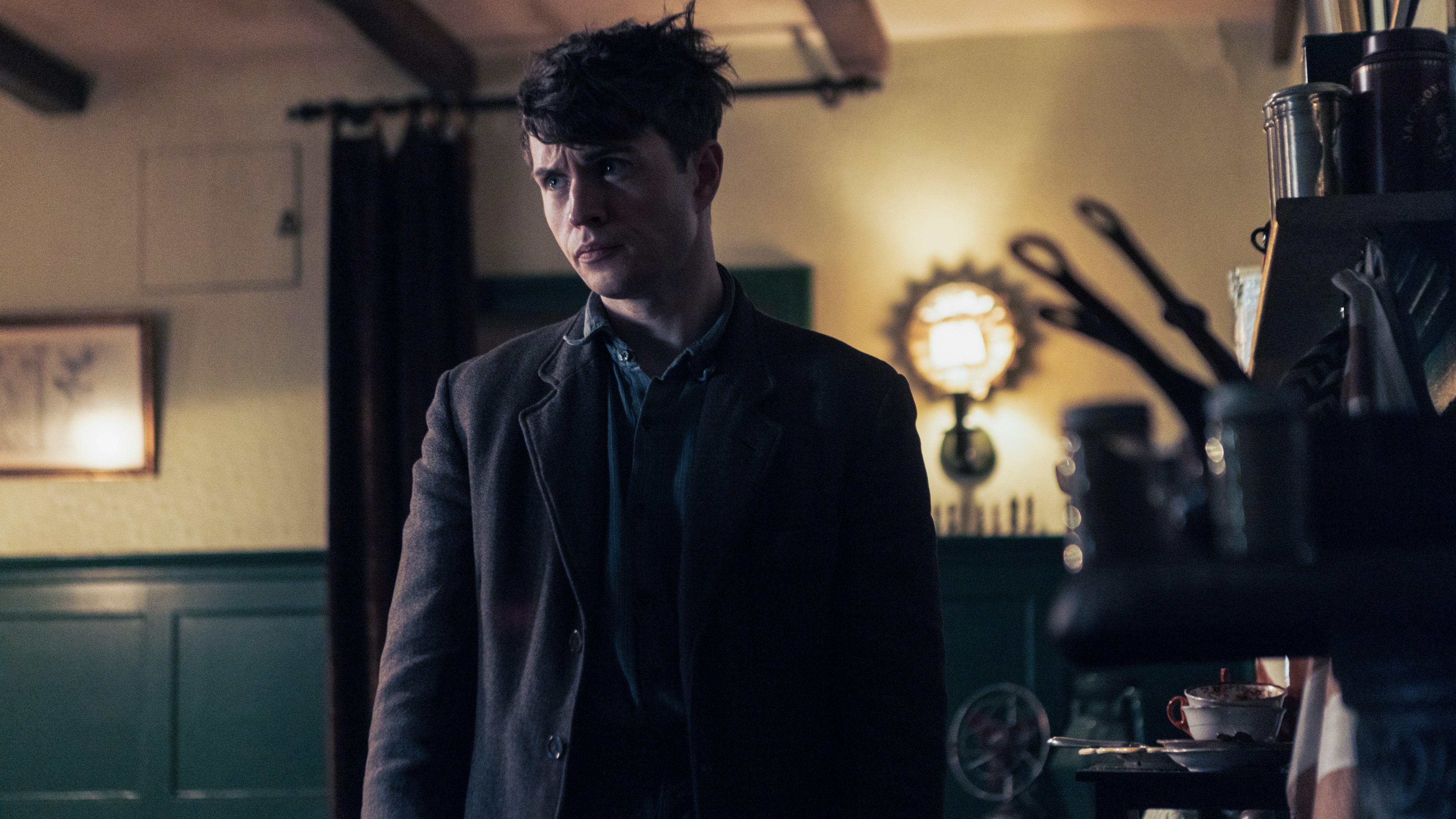 Jack (Connor Finch) stands inside a kitchen looking dishevelled. His expression is somewhat troubled. The background behind him is slightly out of focus but to his left we can see various items of crockery and kitchen utensils.