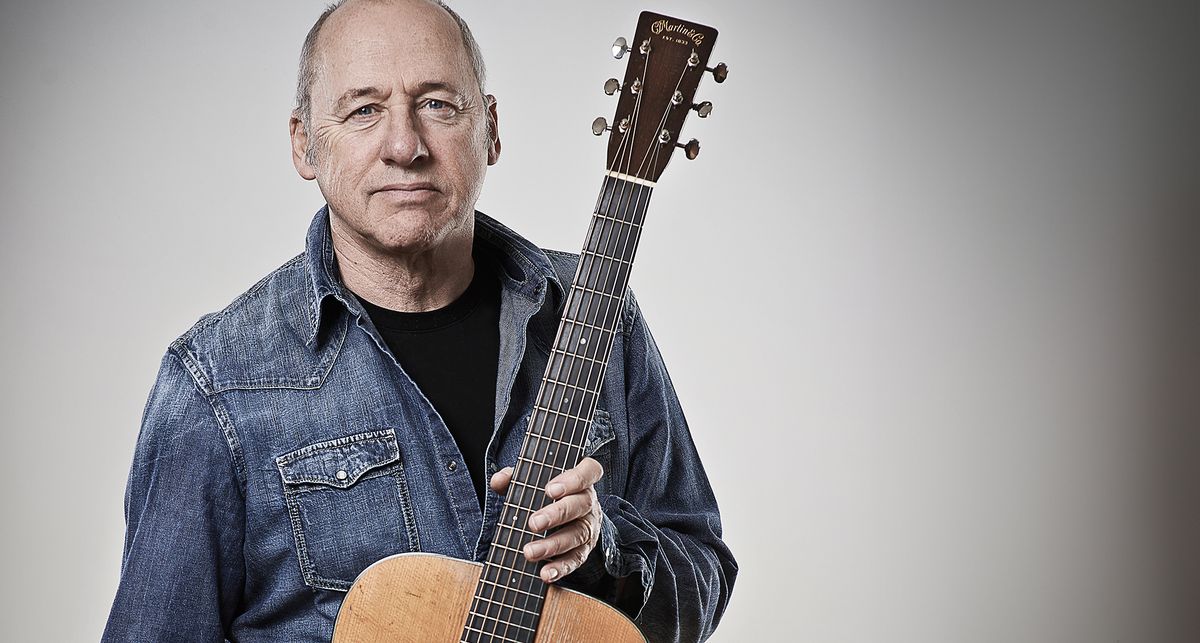 Mark Knopfler wears an old denim short and poses with a Martin dreadnought acoustic guitar