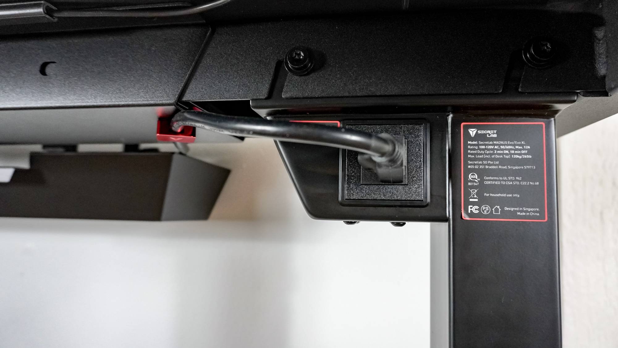 A surge protector plugged into the power outlet at the top of the Secretlab Magnus Evo's leg