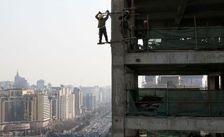 A Chinese migrant worker stands on precarious scaffolding high above the ground