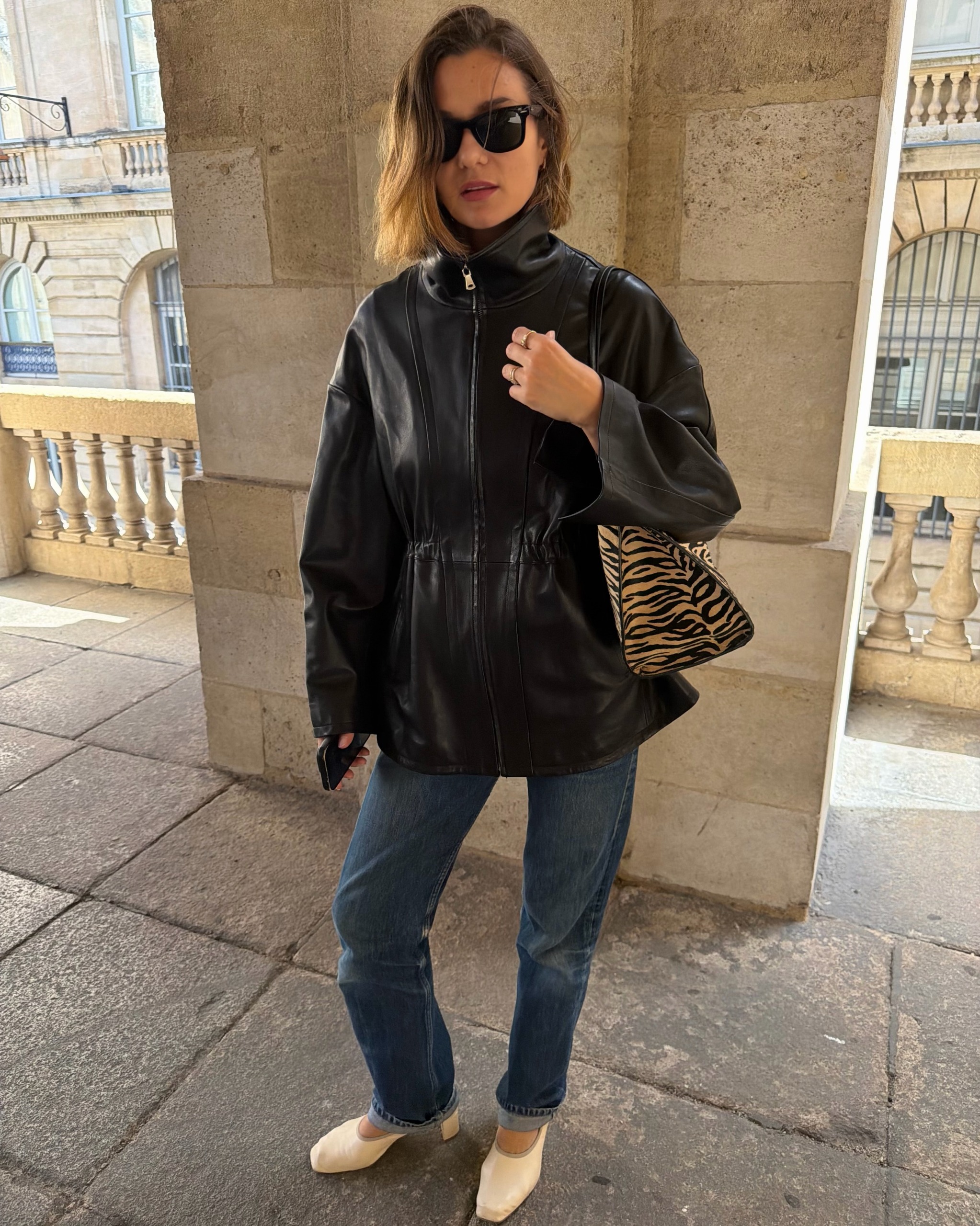 Influencer @annelauremais wears a black leather jacket with blue jeans, white heeled shoes and a tiger print bag.