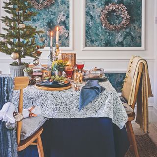 A dining room with the table decorated for Christmas with a small Christmas tree, lit candles and pinecones