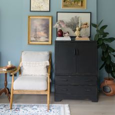 A blue-painted living room with vintage artwork on the walls and a vintage cabinet painted matte black