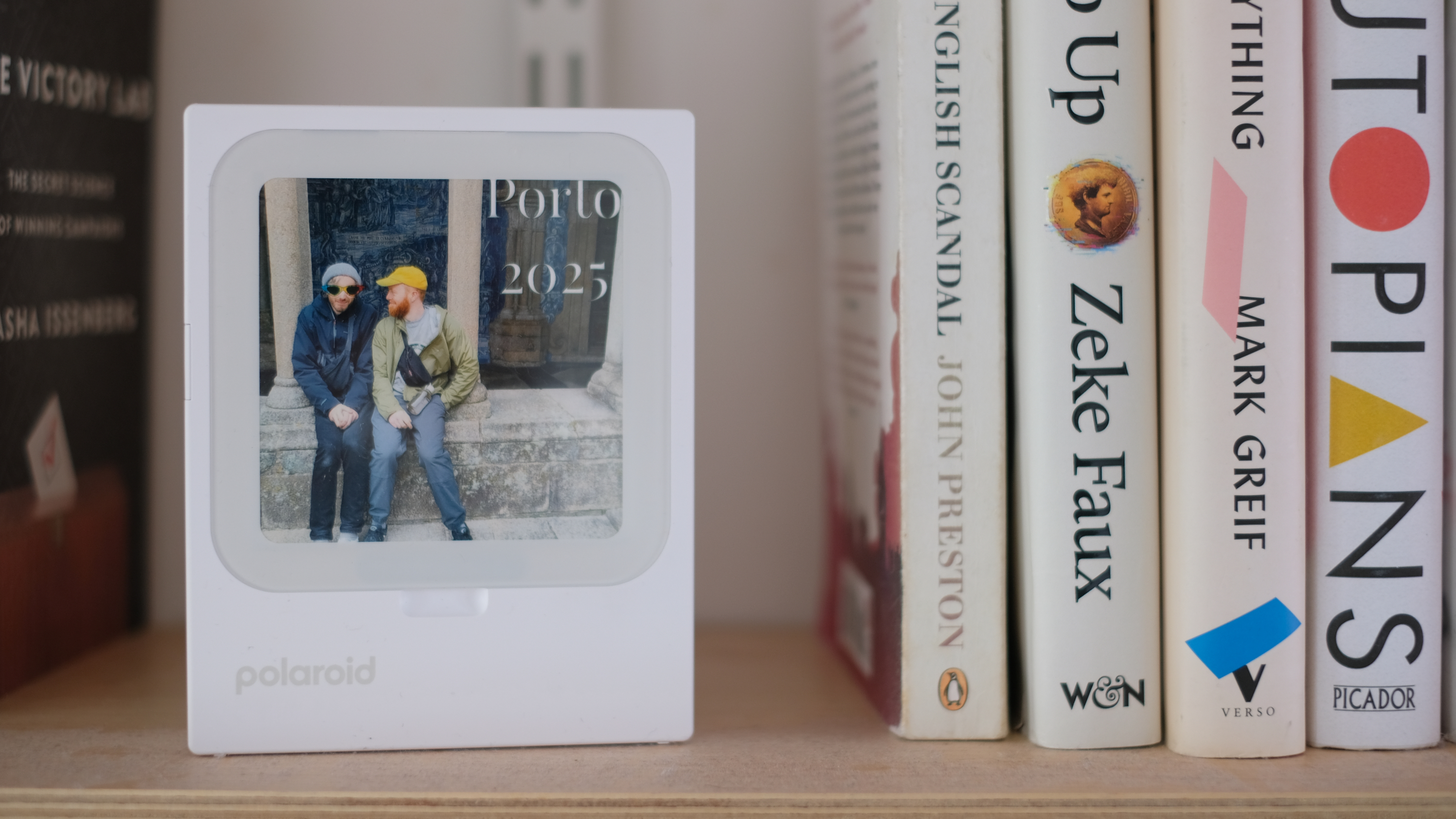 Photograph of Polaroid Hi-Print 3x3 mini instant printer displaying a photo of two friends sitting on a wall, with the text 'Porto 2025' added
