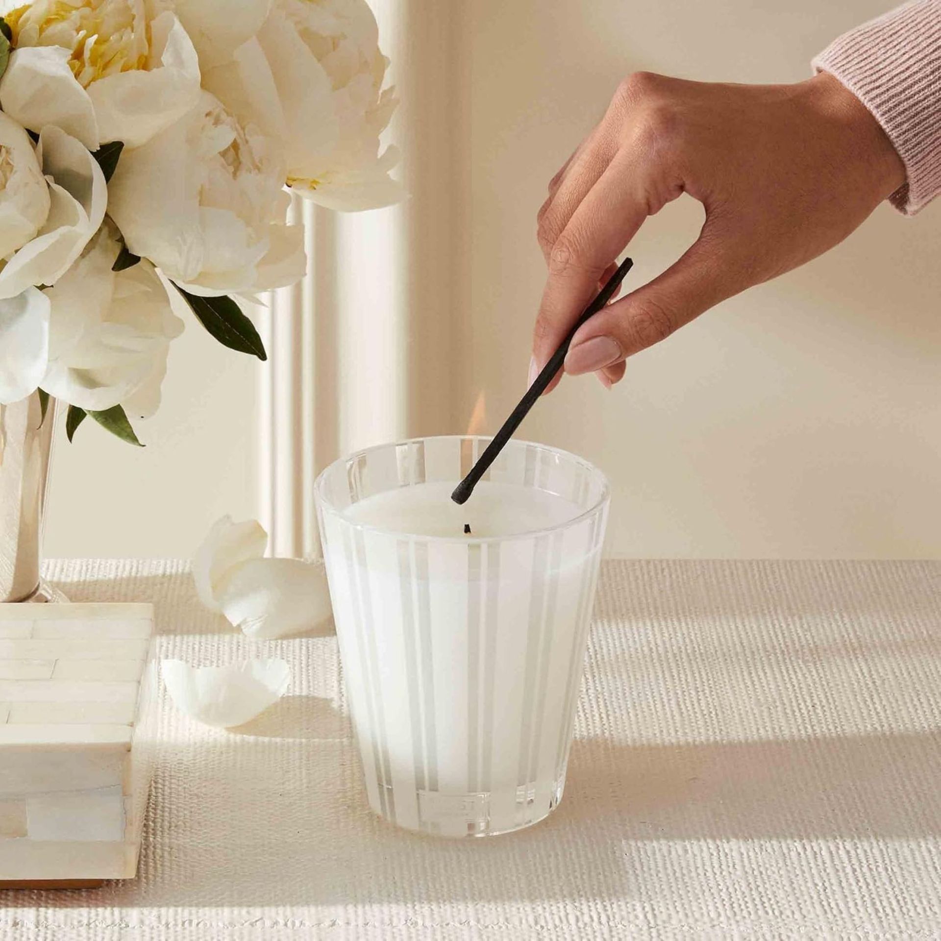 A hand lighting the NEST Fragrances Linen Scented Candle against a cream background.