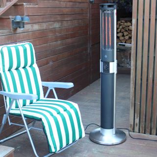 The Swan Column patio heater in an outside space with a green and white striped patio chair
