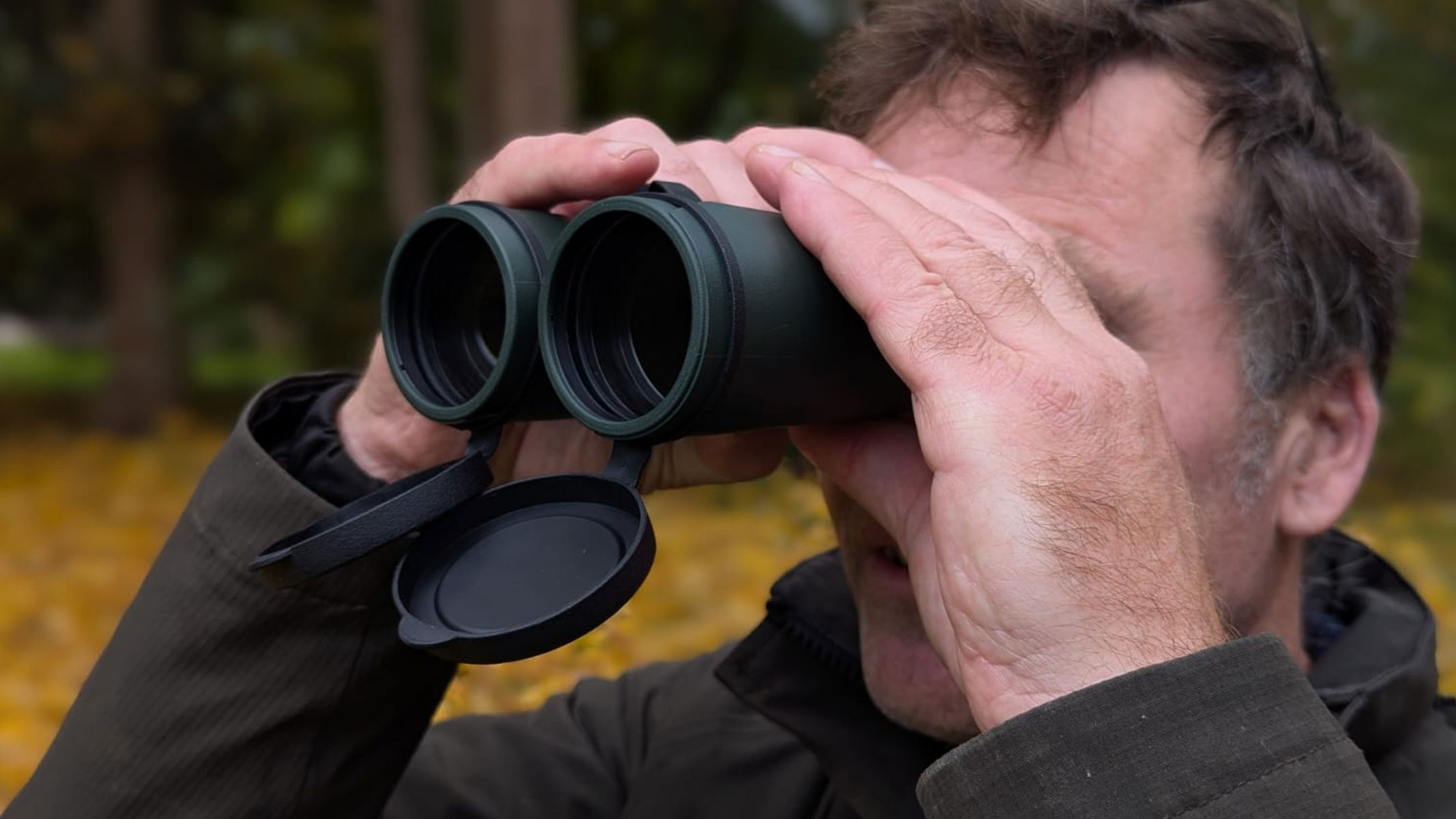 A close up of the objective lenses of the Carson VX 12x50 binoculars as our reviewer is using them. Autumn leaves are on the ground in the background.