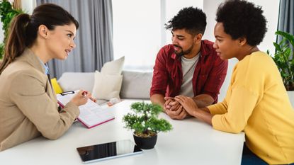 A financial adviser and a couple sit at a table looking at paperwork.