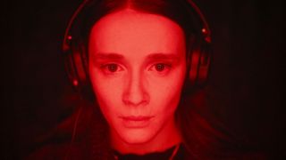 a woman in head phones stares at a screen lit by red lighting in a still from the movie red rooms