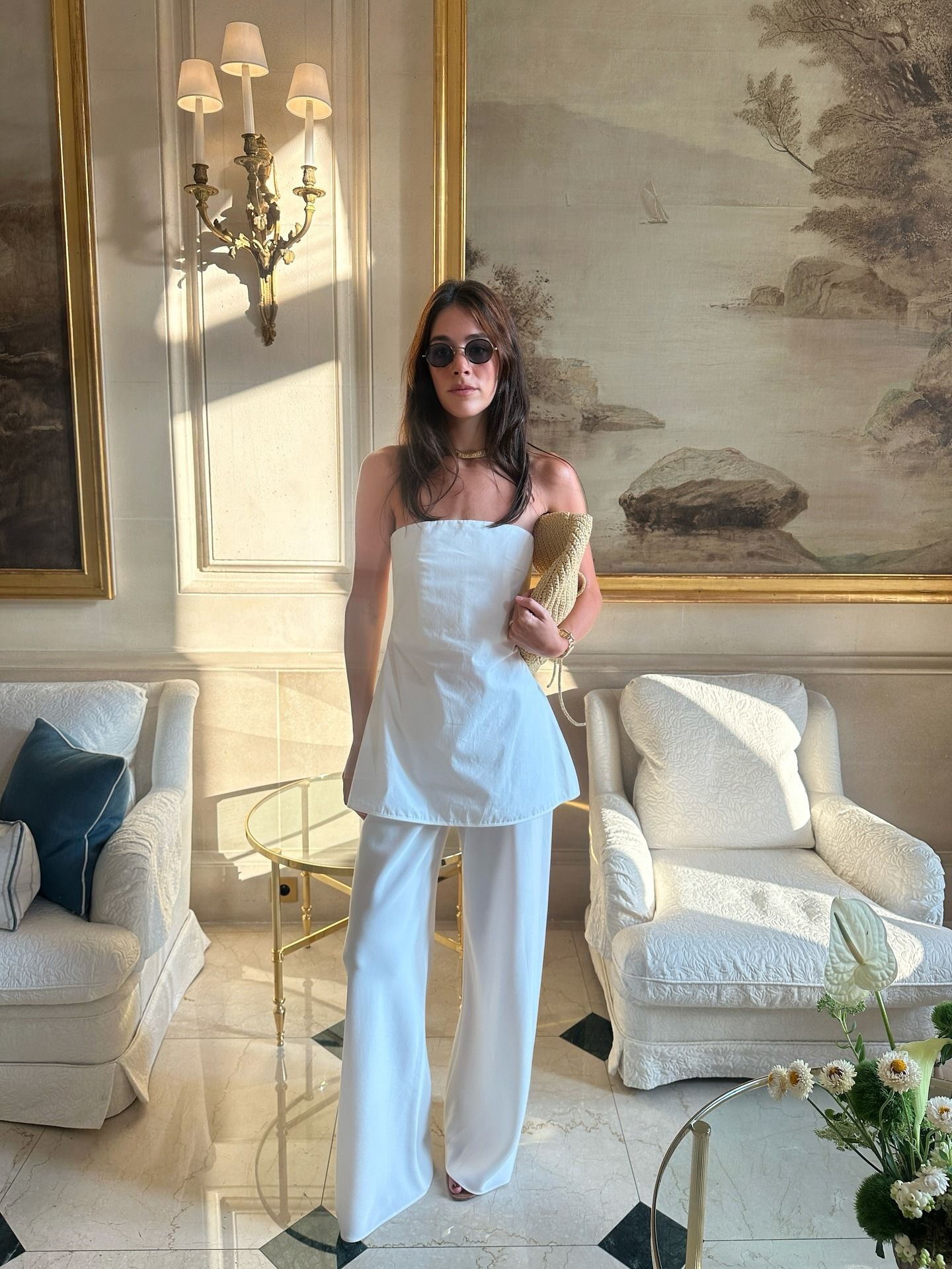 Ilana wears a strapless white top, white pants, and raffia clutch.