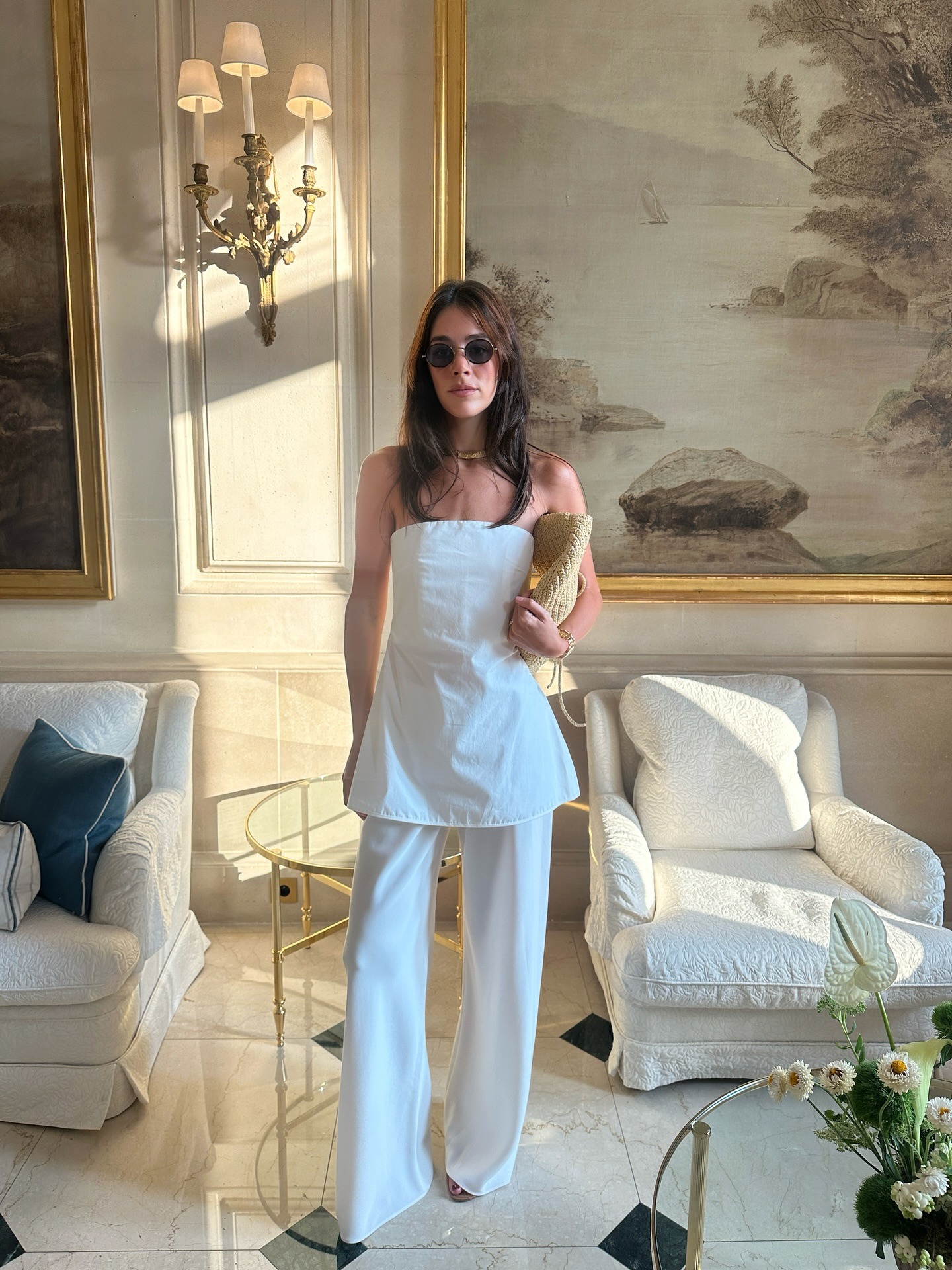 Ilana wears a strapless white top, white pants, and raffia clutch.