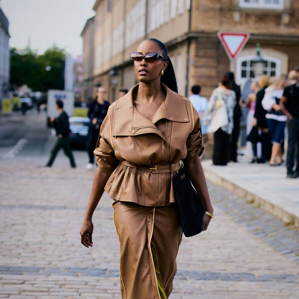 Woman wears cropped tan trench and matching skirt with a handbag as she walks through the street. 