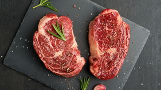 Uncooked steak on slate board with rosemary and garlic