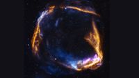 A circular array of blue and pink and orange gas swirls against a dark starry background