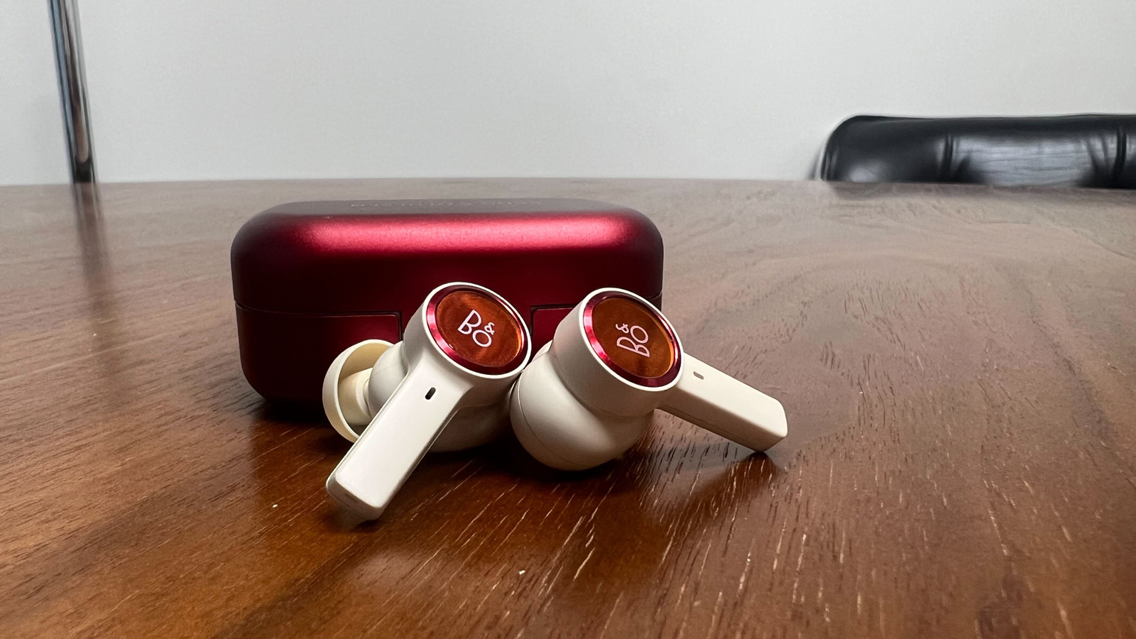 B&O Beoplay EX in Lunar Red resting against their charging case
