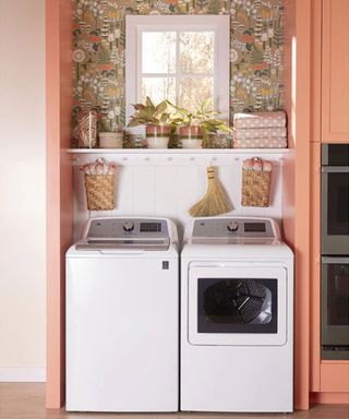 a top loading washer and dryer in a small laundry room with shelving in a kitchen with peach walls