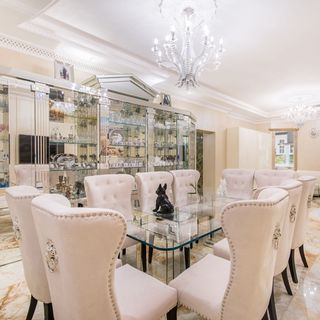 dining room with coral flooring and giant chandeliers with glass dining table and table beneath.