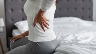 Person sat on mattress indicating they are suffering back pain - a reason why you should change your mattress