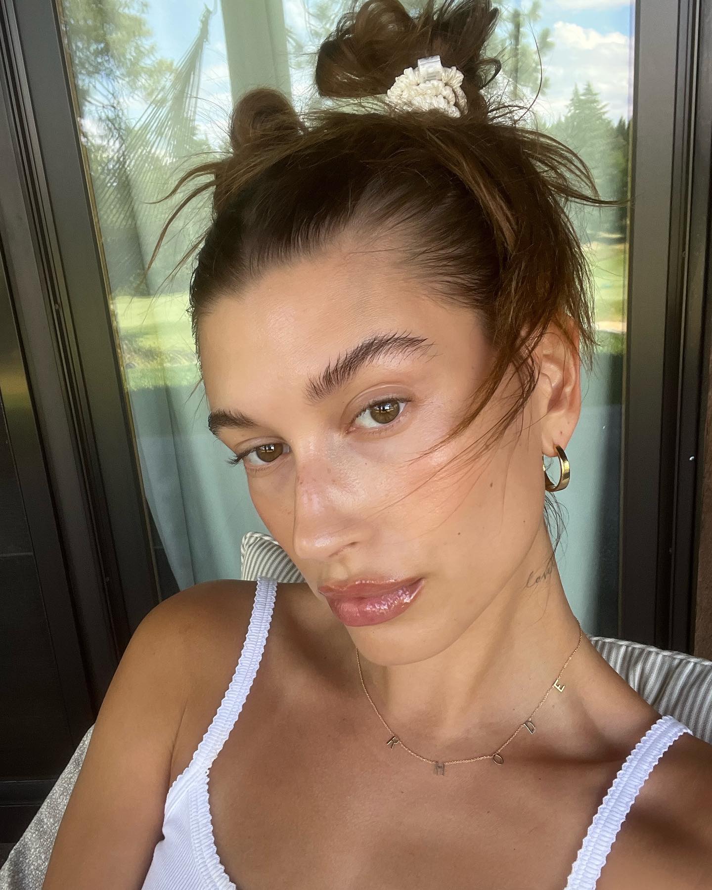 hailey bieber in a white lace tank top, two space buns, and glowing skin with hydrated lips