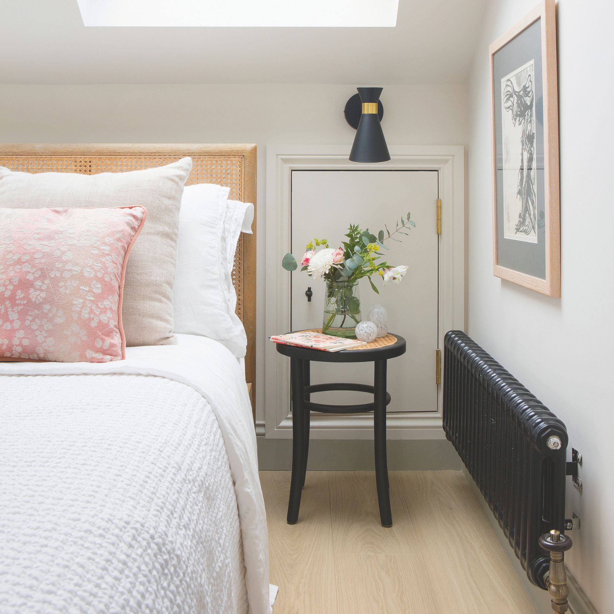Black radiator in bedroom with rattan headboard, pink floral cushion and black stool bedside table