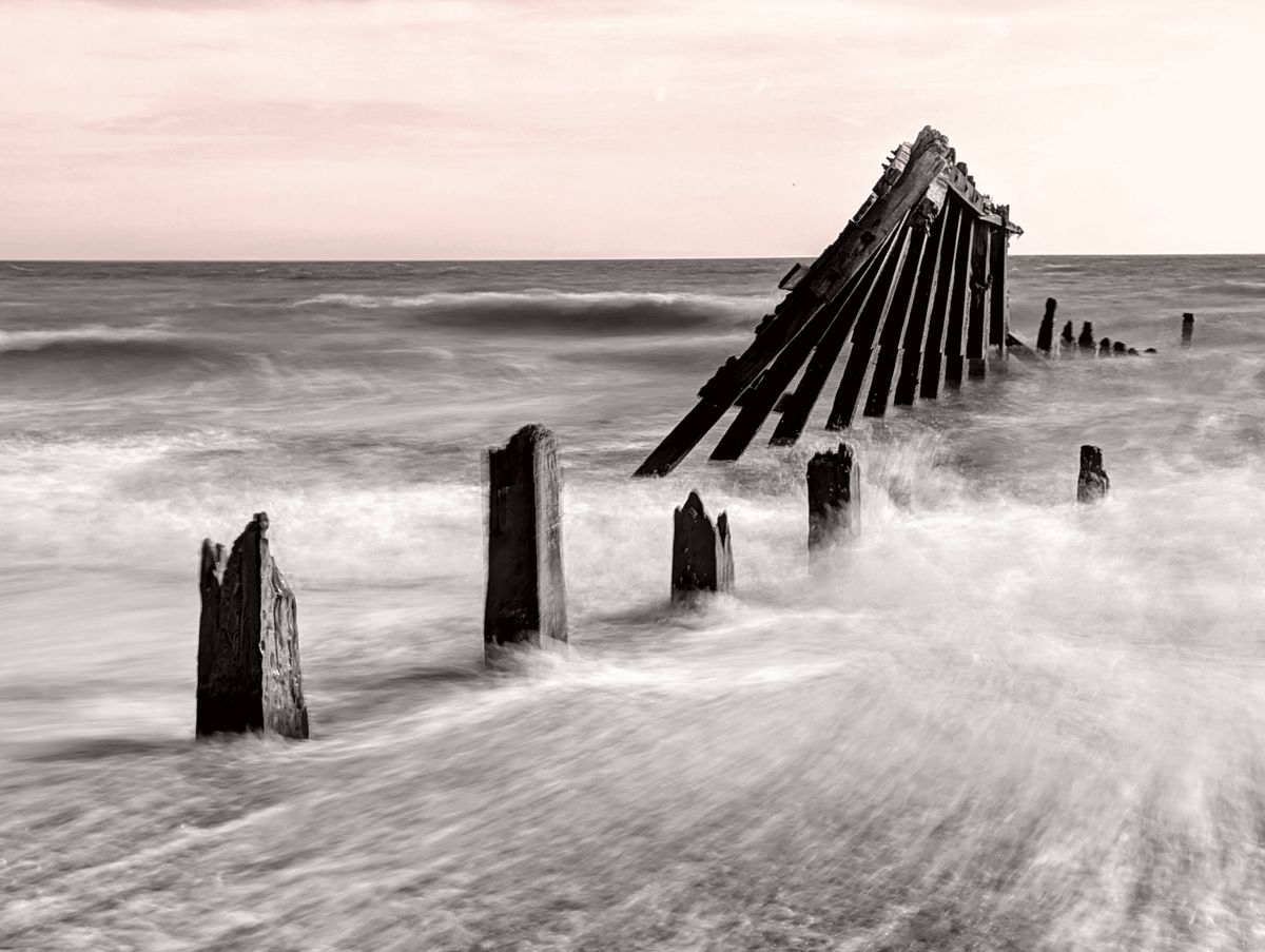 A damaged groyne on a UK beach, the high tide is smashing into it, with the moving water blurred using a long exposure photography technique